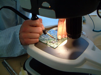 Danish student uses a microscope to solder together components for the on-board computer