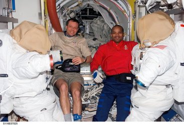Christer Fuglesang and Robert Curbeam inside the Quest airlock with the American EVA suits