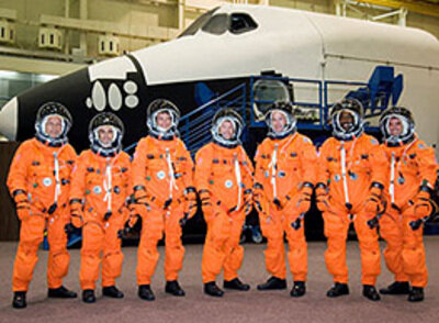 Bemanningsleden van STS-122, inclusief de ESA astronauten Hans Schlegel en Léopold Eyharts. Rechts: STS-122 Missie badge.
