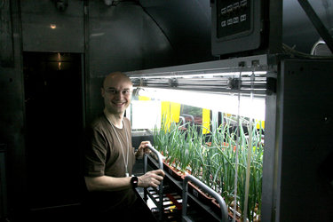Cyrille with the crops growing in the facility's greenhouse